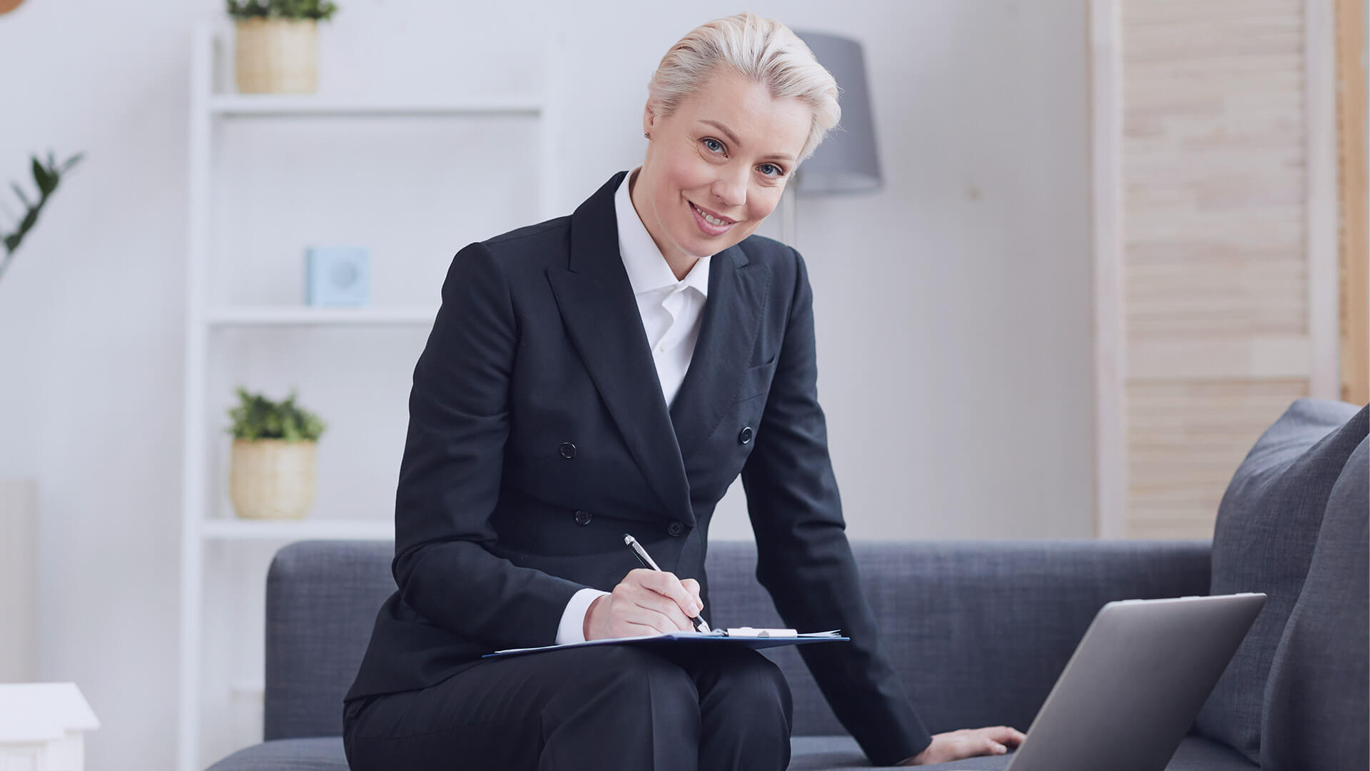 Businesswoman taking notes in a modern office setting with laptop.