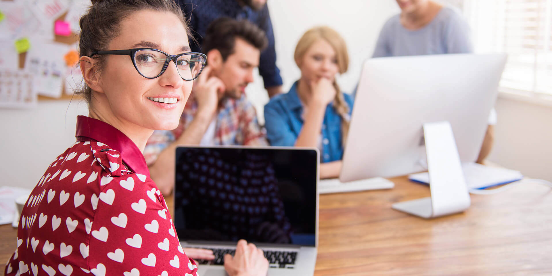 Team collaborating around a laptop and computer, possibly discussing website hosting options.