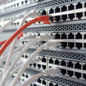 Network switch with white and orange ethernet cables plugged into ports.